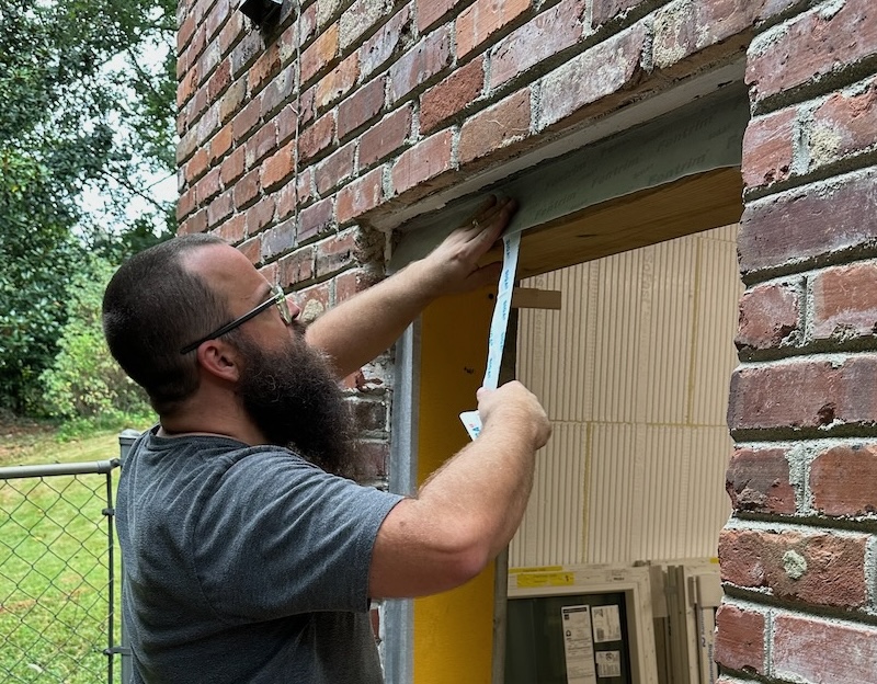 Builder Ben Bogie putting Siga flashing tape on a window opening